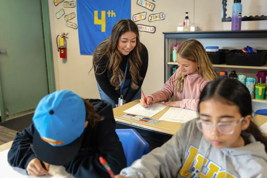 Mujer supervisa a estudiantes en un salón de clases.