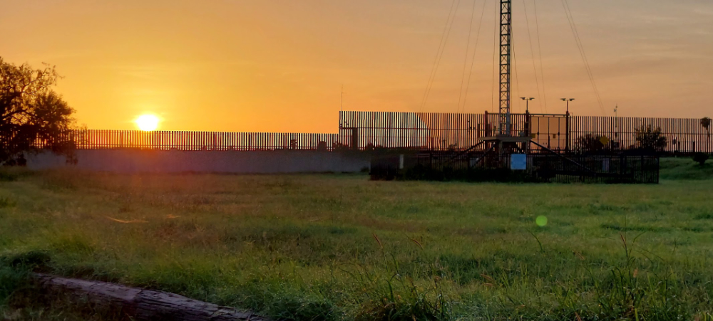 a fence and grass field with a sunrise