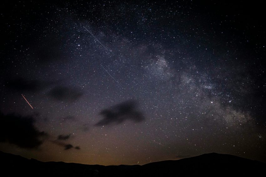 A stunning night sky showcasing stars, clouds, and the Milky Way galaxy with a visible meteor shower.