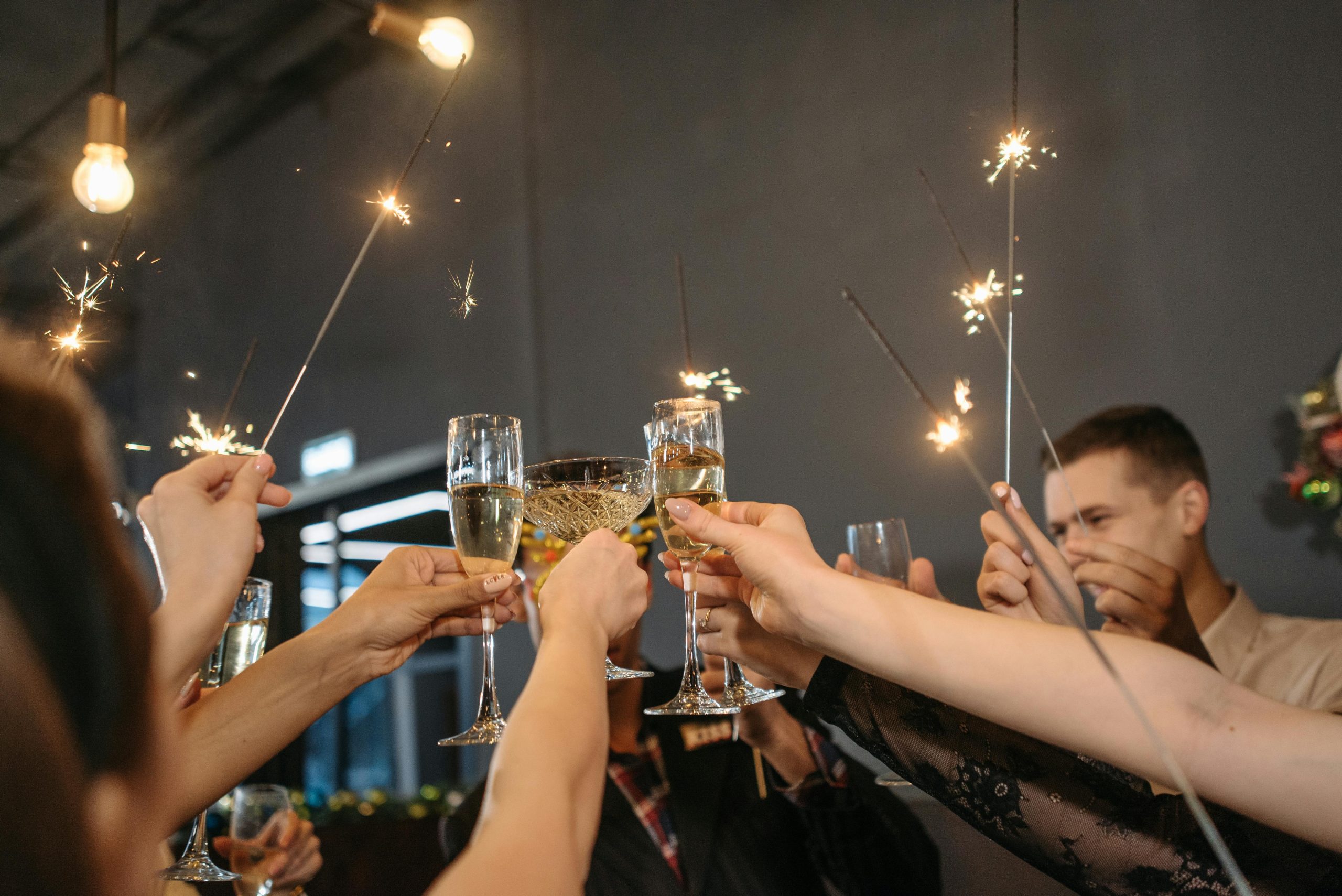 Tradiciones de Año Nuevo: Coloridos rituales llenos significado para comenzar el año Group of adults celebrating with sparklers and toasting champagne indoors.