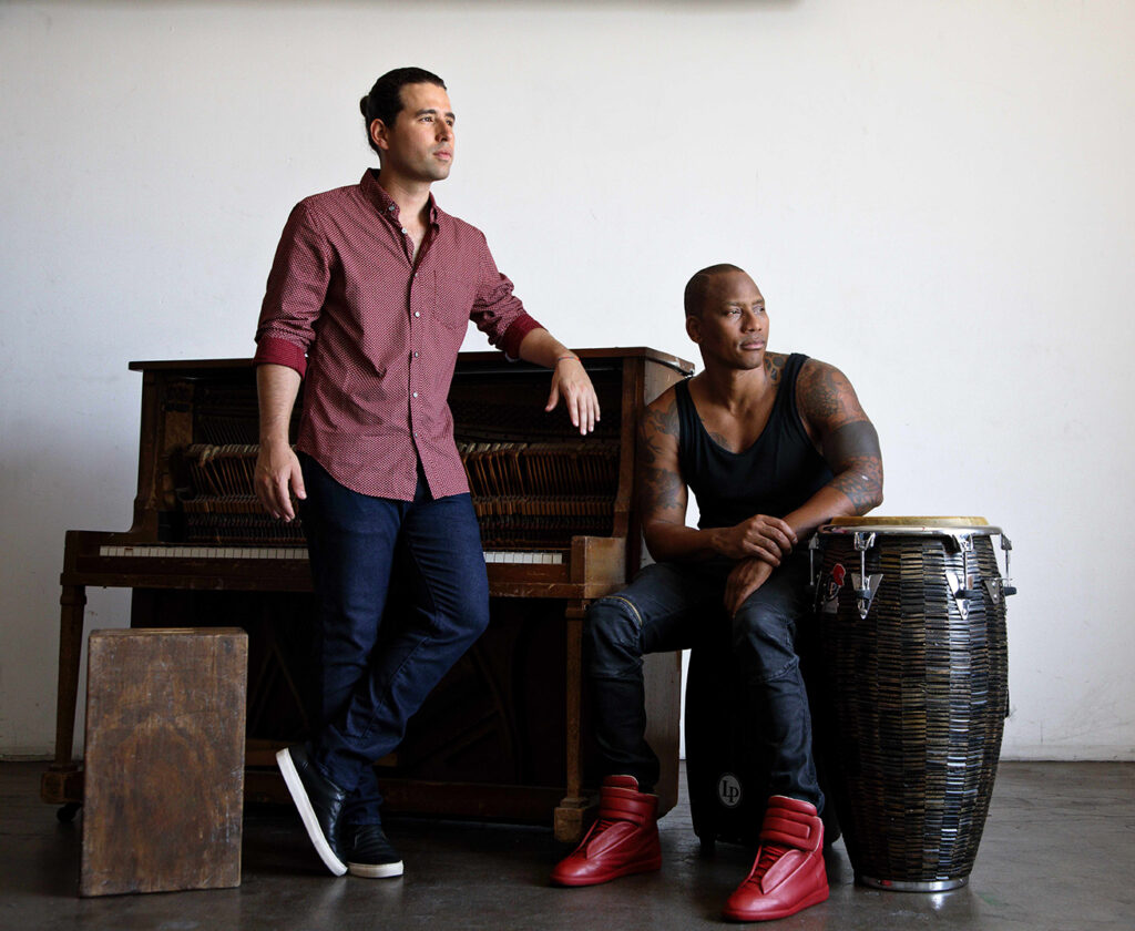 Dos hombres junto a piano y bongó